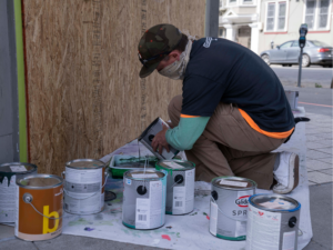 SF Artist, Todd Kurnat, mixing paints in front of boarded up Goodwill store on Haight St