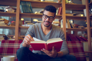 Smiling-guy-reading-a-book-in-a-library
